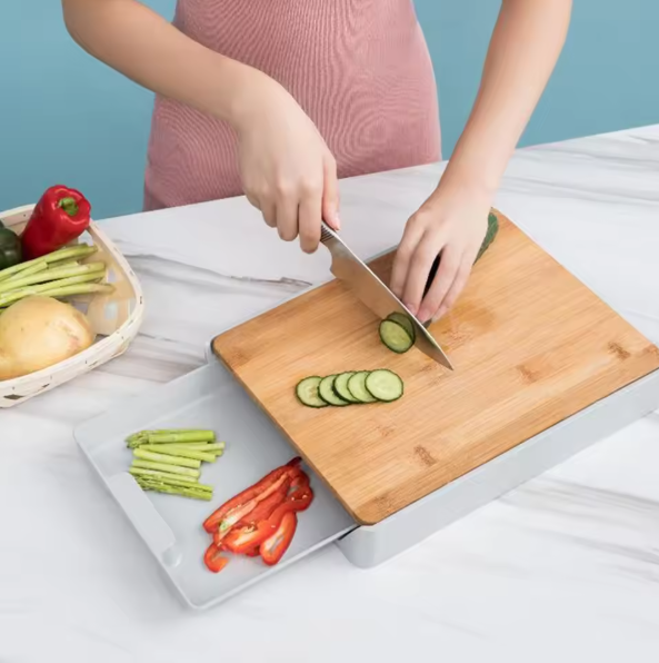 Person slicing vegetables on a Bamboo Cutting Board With Drawer with a blue background