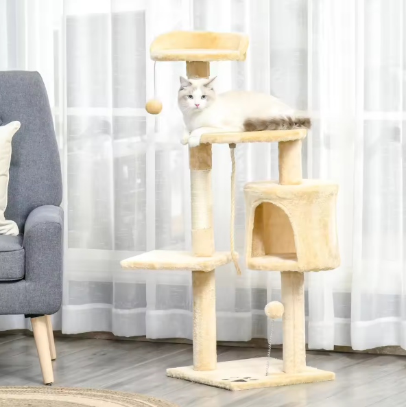 Cat sitting on a multi-level cat tree in a room with a gray armchair and white curtains.