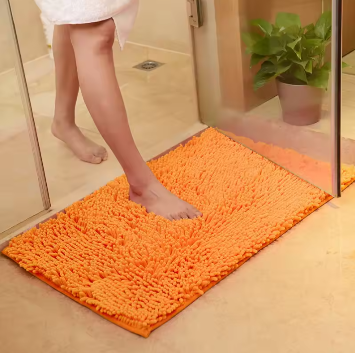 Orange bath mat on a bathroom floor with a person stepping onto it.